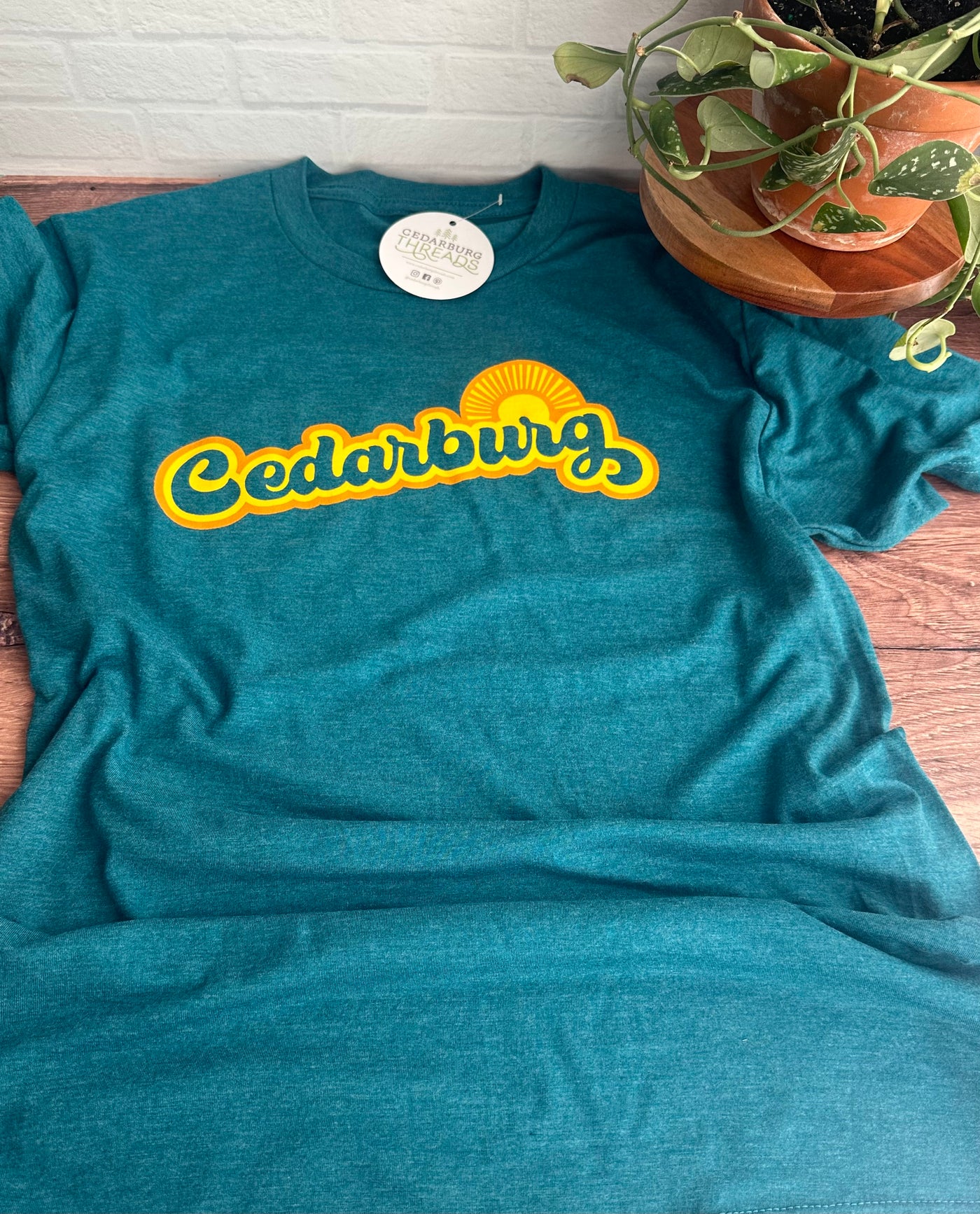 Teal triblend unisex short sleeve crewneck t-shirt with Cedarburg sun design in yellow and orange
