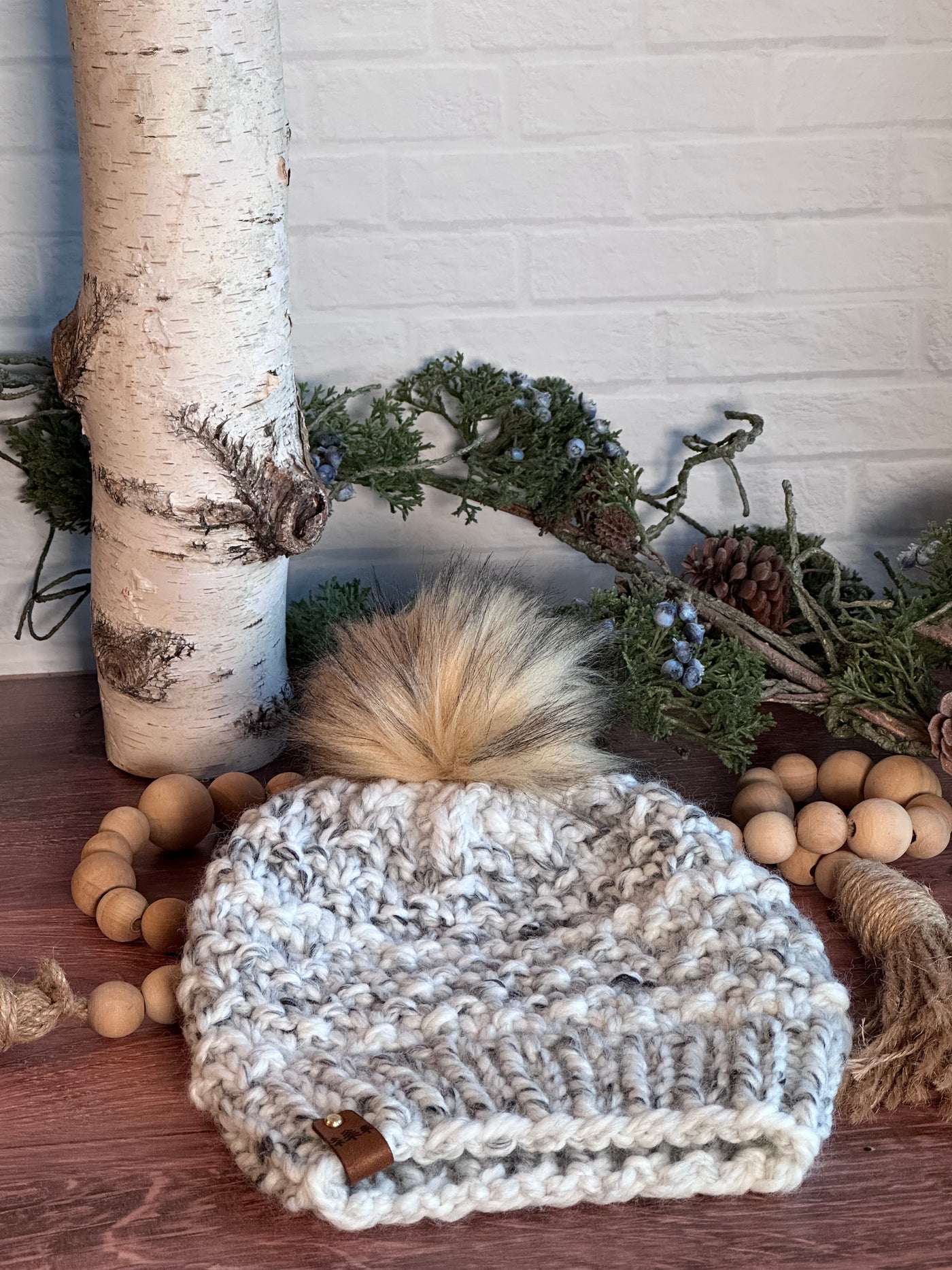 chunky handmade knit hat in charcoal and white colored yarn and a brown faux fur Pom Pom